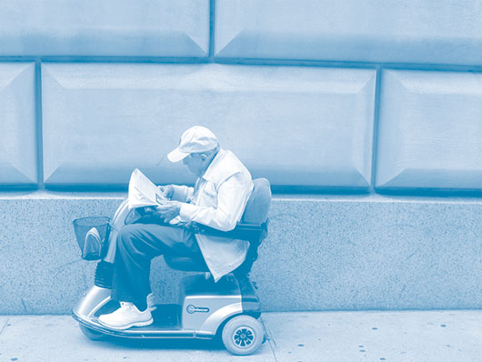Photo of an elderly person reading a newspaper travelling in mobility scooter
