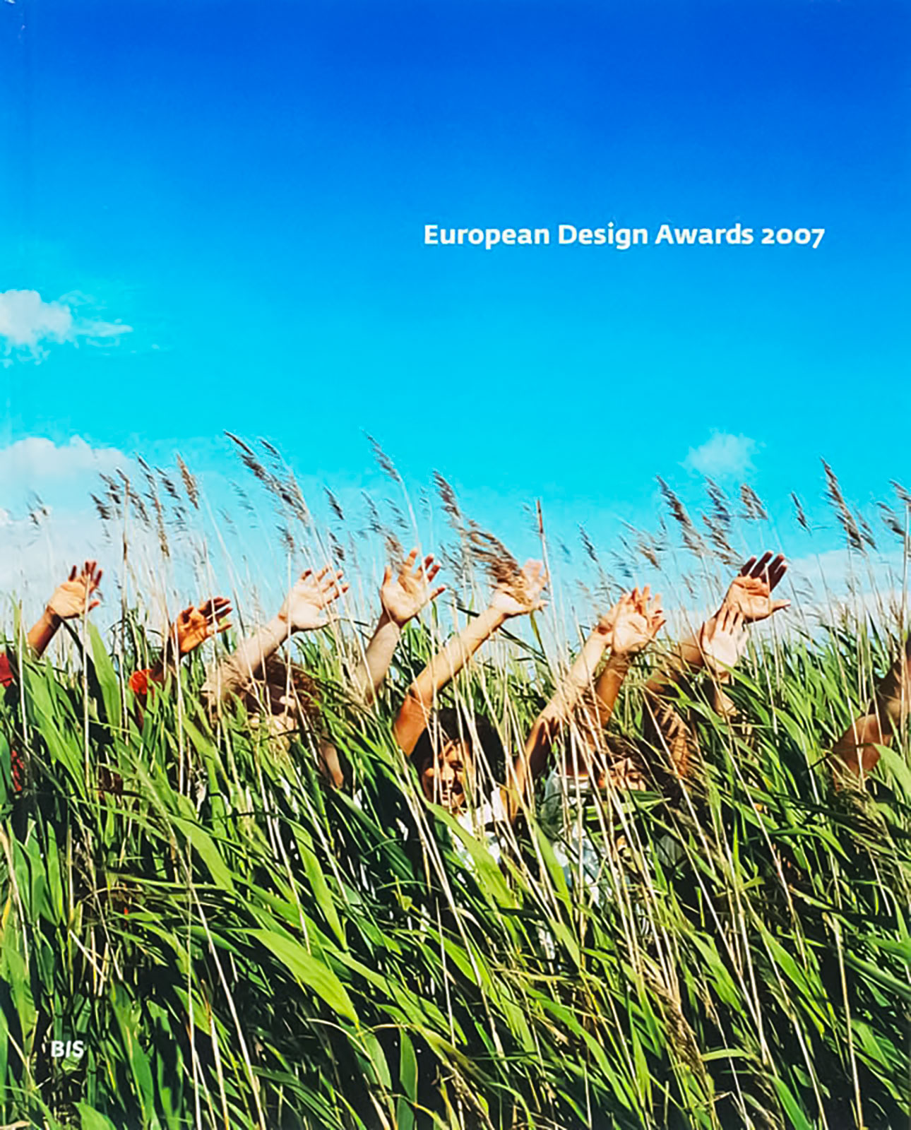 Book cover of the European Design Awards annual. Shows a large blue sky with green grass below, and people standing in the grass with their hands waving and swaying left to right