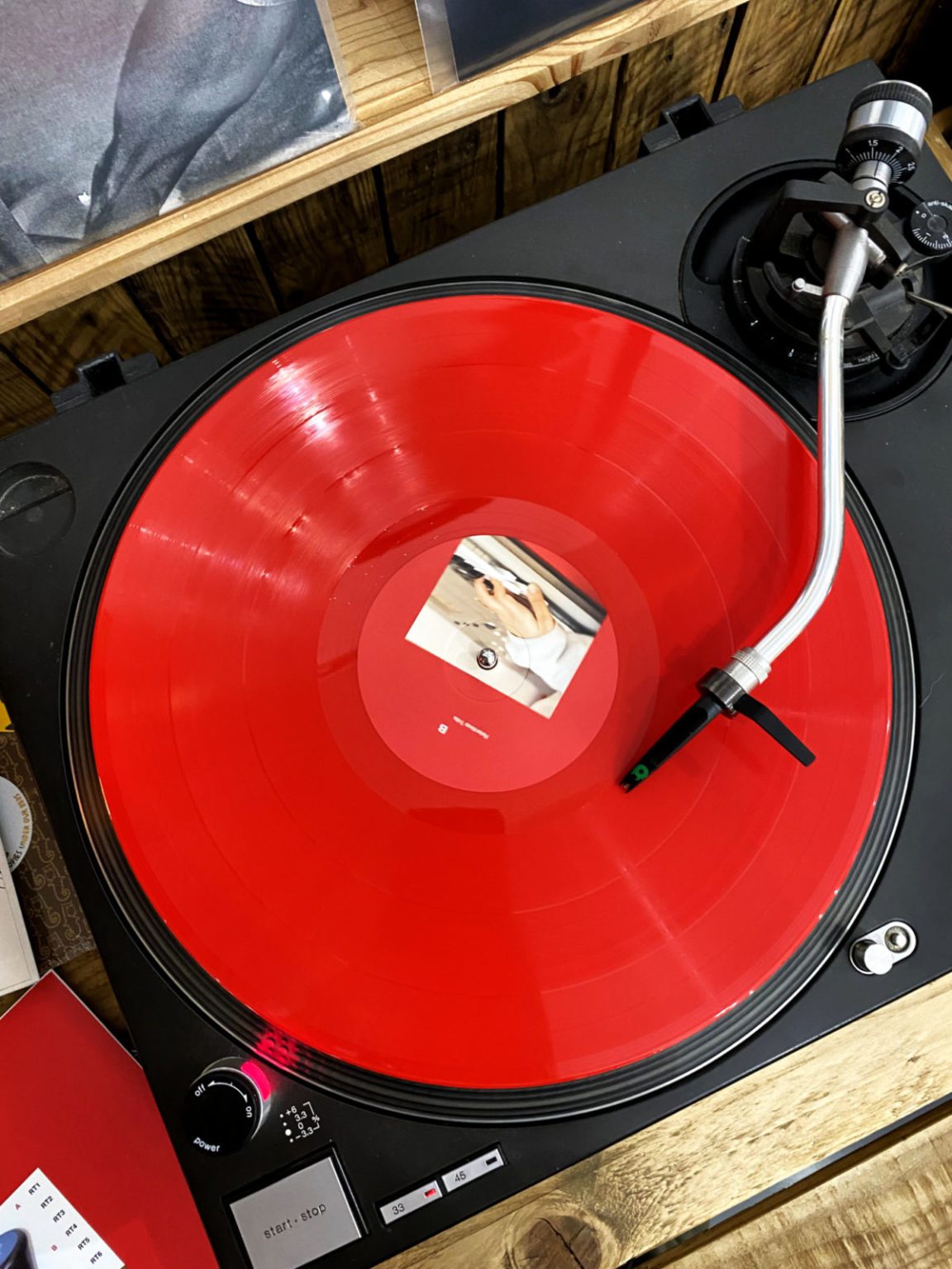 A vinyl DJ deck, shows the metal arms, then a red vinyl on the deck spinning round