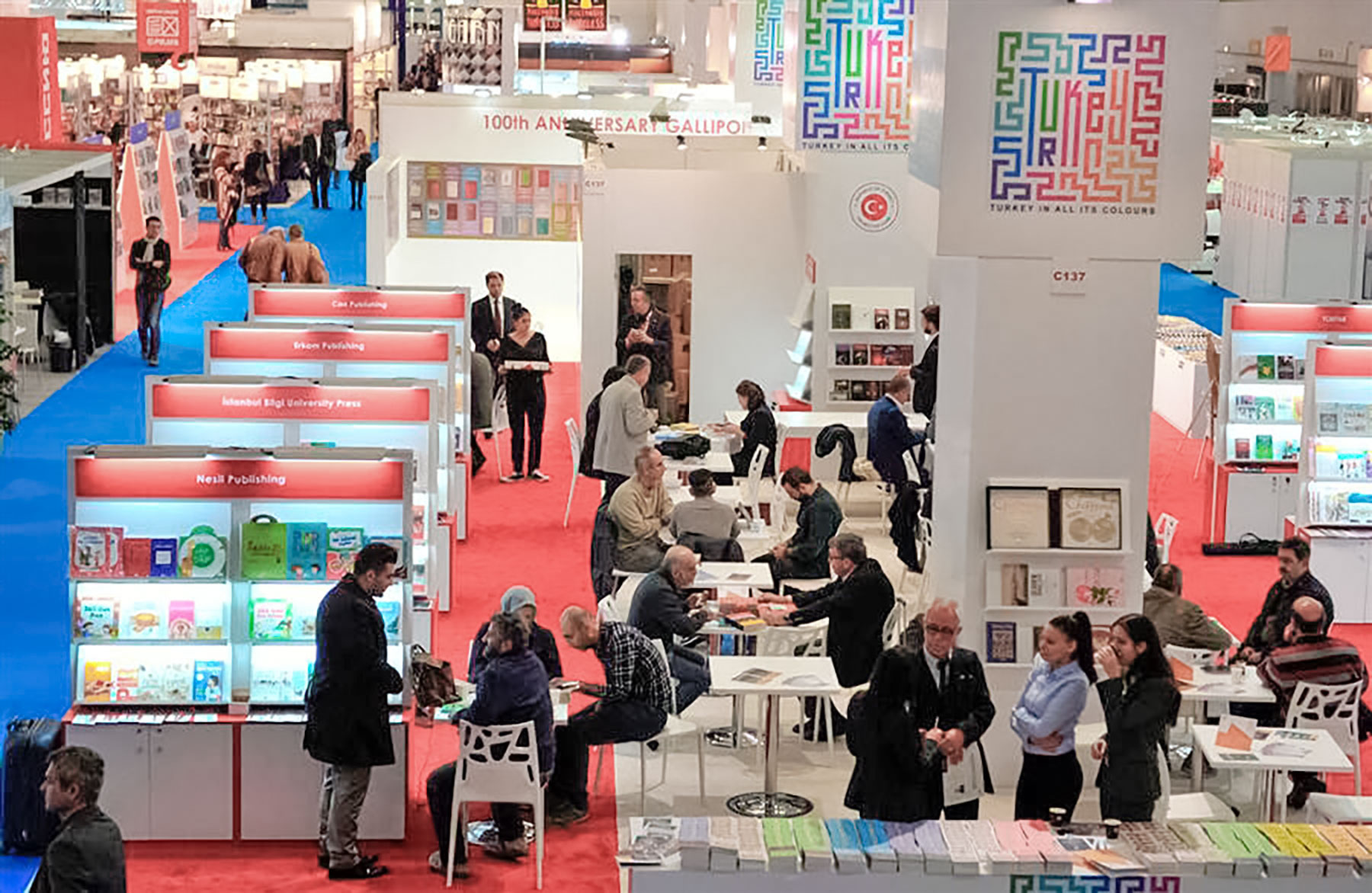 Photo of an exhibition hall at the Frankfurt Book Fair. Shows exhibition stands and small tables with people having meetings