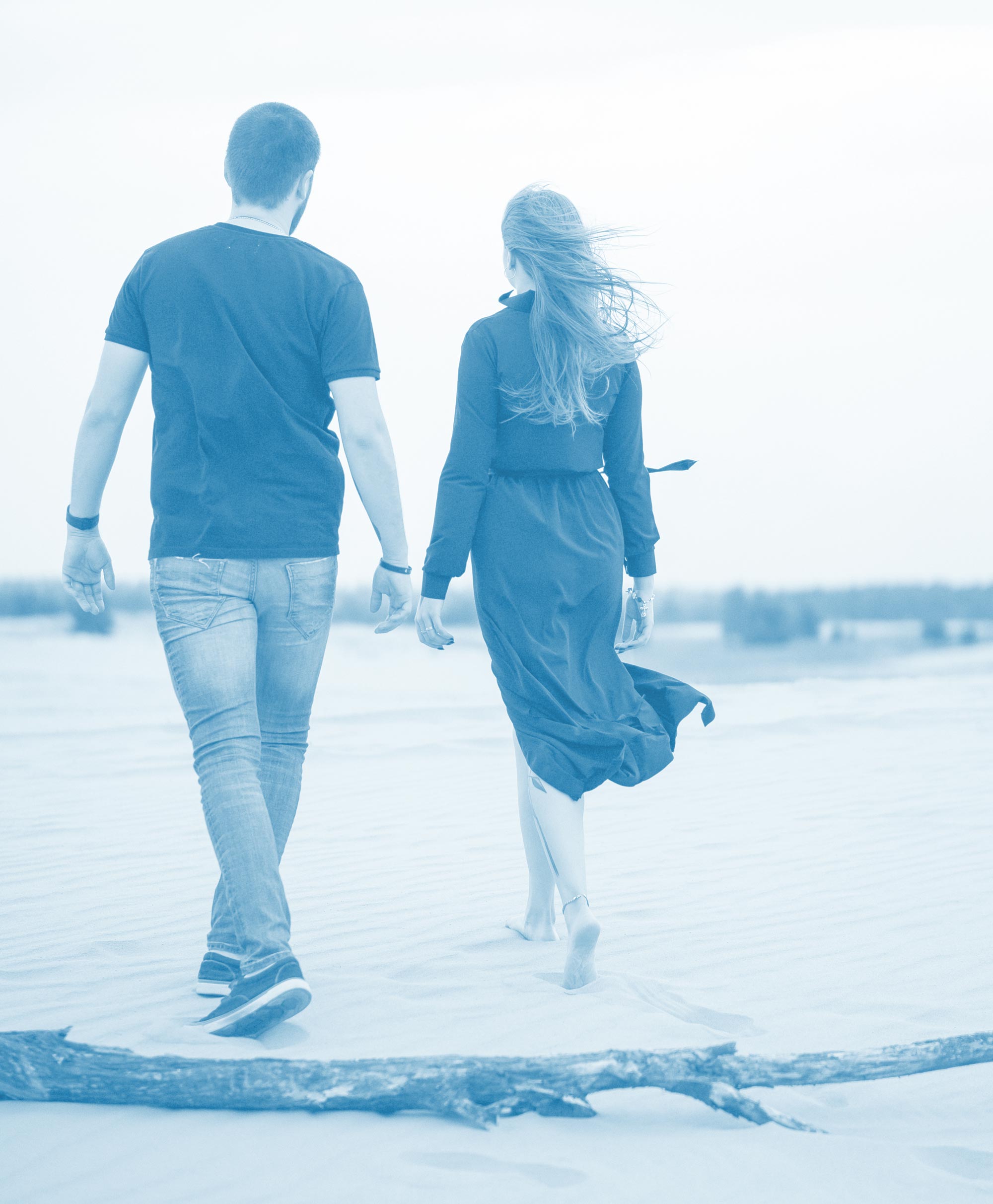 Man walking on the left and woman on the right, down the beach, their hands in the middle are nearly touching.