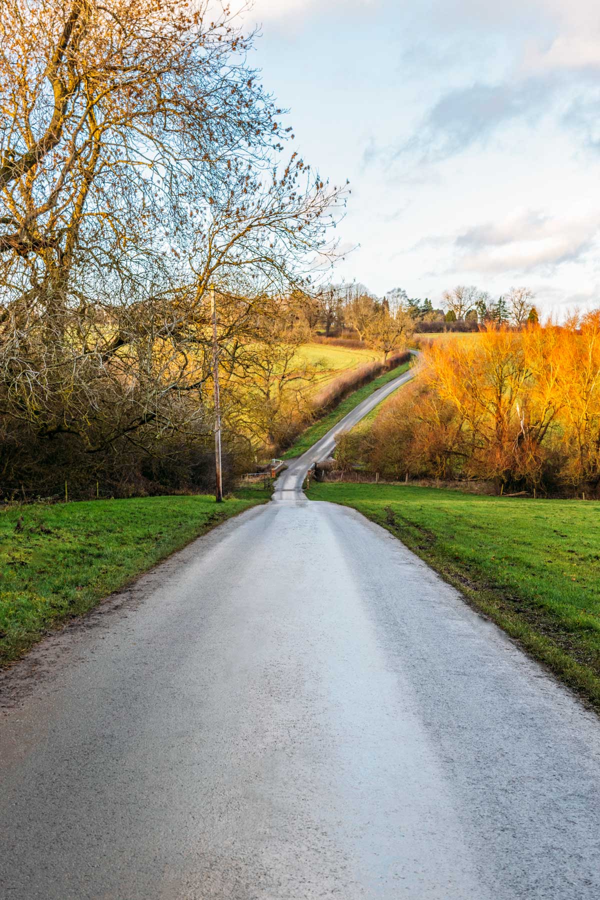 Photograph of a steep country lane with road going through the middle then rising into the distance. Blues, yellows and greens have satuartion emphasised