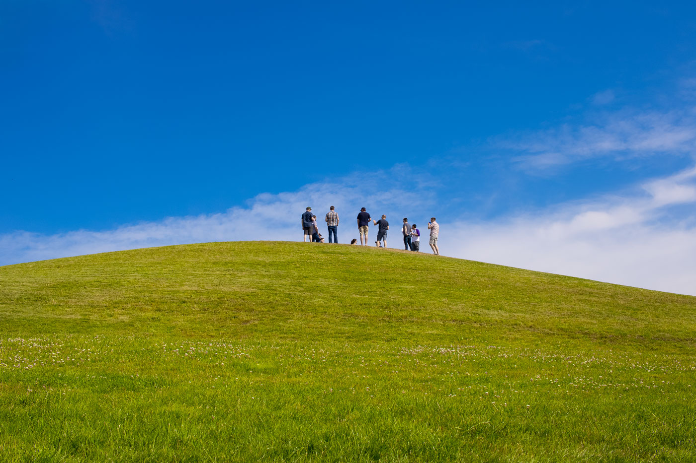 Original photo of a green hill in the front and blue sky in the background with a group of people standing on the top of this hill. No colour grading applied