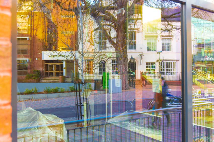 Shows that start of lower New Walk going under an iron gate feature, with buildings and trees on the left and right