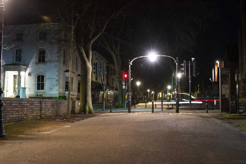 Photography at night time of half-way down New Walk, showing the Belmont Hotel on the left, with cars whizzing across. Shows a bright street light
