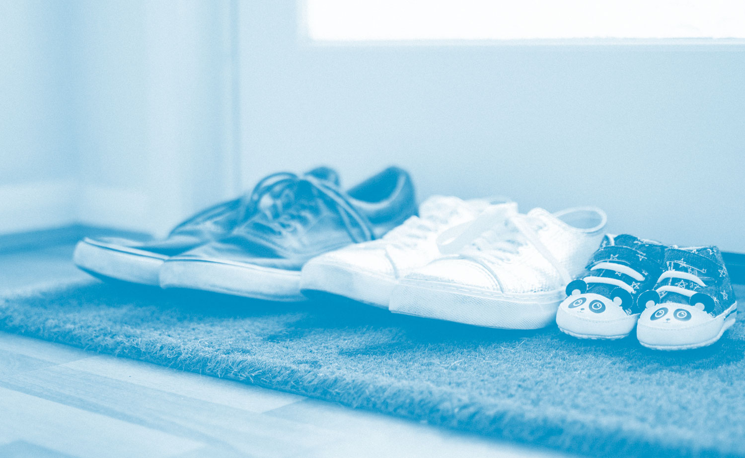 Photo of a doormat then 3 different pairs of shoes on top of it. On the left are a man's shoes, then in the middle are a woman's shoes, then on the right a kid's shoes